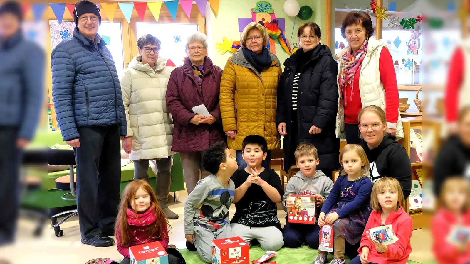 Die Kinder wussten genau, was Tonie-Boxen sind und wollten alles gleich auspacken. Kindergartenleiterin Theresa Schiller (vorne, rechts, knieend) und Pfarrer Berthold Heller (links) freuten sich über die Geschenke, die FU-Vorsitzende Renate Müller (Dritte von rechts) und ihre Vorstandsdamen mitgebracht hatten. (Bild: wlr)