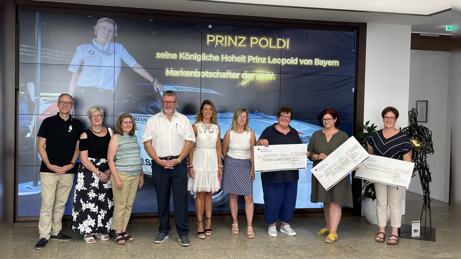 Im Bild von links: Bürgermeister Bernd Sommer, Gudrun Sirtl/KAB, Gabi Treml-Laubert/2. Vorsitzende OGV Waldsassen, Klaus Schuster/Organisator, Sandra Winter/Vertreterin des Hauptsponsors, Doris Wagner-Zeeh, Karin Borchers, Barbara Schmid, Sonja Schnurrer; im Hintergrund an der TV-Wand der Ehrengast der Veranstaltung: seine Königliche Hoheit Prinz Leopold von Bayern mit seinem BMW M1.<br> (Bild: Klaus Schuster)