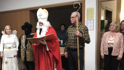 Der Heilige Nikolaus, Knecht Ruprecht und Engelchen besuchten die Senioren vom Markt Schwarzenfeld. Den heiligen Stab vom Nikolaus durfte der Senior Prebeck Rudi aus dem Publikum, den der Nikolaus ausgesucht hat halten, die Seniorenbeauftragte Gabriele Beck (links) hörte im Hintergrund dem Rückblick vom ganzen Jahr zu. (Bild: Silvia Beck)