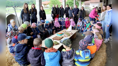 Nach der Besichtigungsrunde durften die Kinder am gedeckten Tisch Platz nehmen. Leckeres vom Bauernhof spendierte die Familie Salomon. Im Bild hinten stehend von rechts die Bauernhofbewirtschafter Maria und Martin Salomon mit ihren Familienangehörigen und dem Auszubildenden; ganz links stehend die bayerische Milchkönigin Elisabeth Heimerl. (Bild: Josef Böhm)