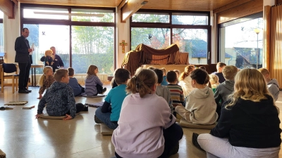 Die Kinder lauschen einem Gespräch zwischen Pfarrer Klausfelder (stehend links) und der Handpuppe Max, gespielt von Andreas Walter (sitzend links im Hintergrund) (Bild: Lisa Barthelmann)