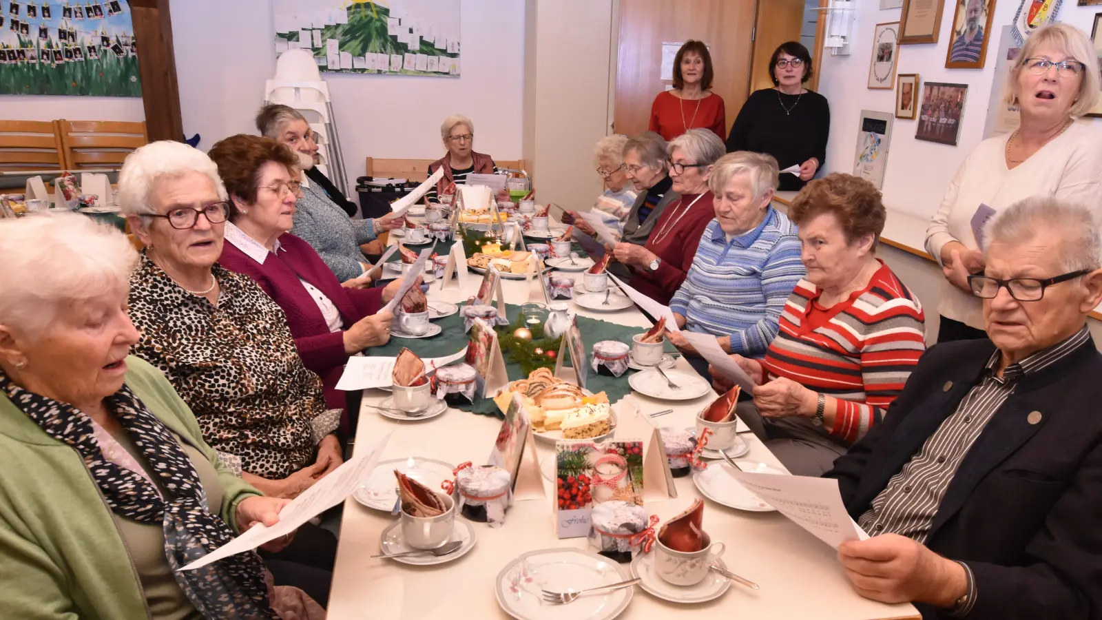 die Senioren, an festlich gedeckten Tischen im evangelischen Gemeindehaus, beim Singen vertrauter Weihnachtslieder; (auf der rechten Seite): Helferinnen des kath. Frauenbunds und des evangelischen Frauenkreises, die sich um das leibliche Wohl der Besucher kümmerten (Bild: Norbert Weis)