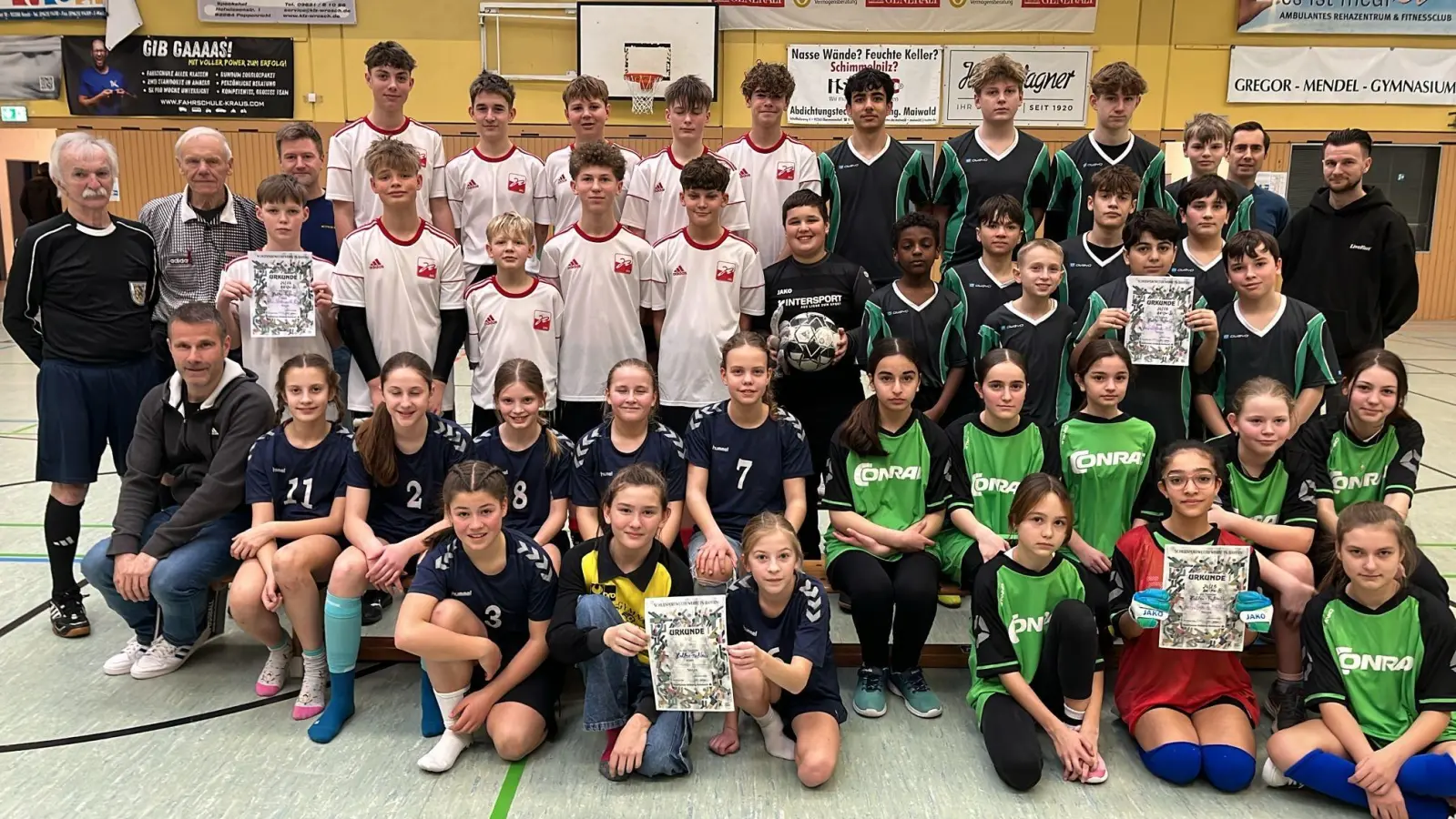 Nach drei Stunden Hallenfußball standen die Titelträger „Stadtmeister” fest. Bei den weiterführenden Schulen siegte bei den Jungs AK-III die Schönwerth-Realschule (weiß) mit Lehrer Johnnes Barthel (3.v.l.) und bei den Mädels der AK-IV das Erasmus Gymnasium (dunkelblau) mit Lehrer Simon Gräß (sitzend 1.v.l.); beim Wettbewerb der Mittelschulen gingen beide Stadtmeisterbezeichnungen an die Mädels (grün) und Jungs (grau-grün) aus dem Dreifaltigkeitsviertel mit Lehrer Philipp Keilholz (1.v.r.). Wichtige Helfer v.l. die Schiris Karl Vollmer und Adolf Binner und Hallen-Organisator Matthias Harbauer vom GMG (2.v.r.) (Bild: Thomas Gebele)