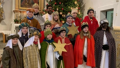 Vierzehn Ministrantinnen und Ministranten aus Flossenbürg sind als Sternsinger verkleidet und stehen im Halbkreis im Altarraum ihrer Heimatpfarrei St. Pankratius Pfarrvikar John Palathinkal hat sie für die Aussendung gesegnet. (Bild: Rebekka Völkl)