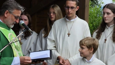 Pater Stanislaus überreicht Taufkreuz und Mini-Ausweis. (Bild: mas/exb)