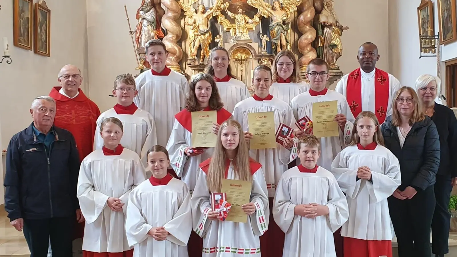 Die verabschiedeten Ministranten mit ihren Urkunden: 1. Reihe vorne: Bianka Saller, 2. Reihe von links: Sarah Scheuerer, Juliane Krafczyk, Daniel Bodensteiner, zusammen mit weiteren Ministrantinnen und Ministranten, Pfarrer Herbert Rösl (2. Reihe hinten links), Pfarrvikar Kenneth Onuoha (hinten rechts), der Ministrantenbeauftragten Christiane Hammer (2. Reihe rechts), Mesner Josef Pflug (2. Reihe links) sowie Mesnerin Elisabeth Dietz (hintere Reihe rechts).  (Bild: Christiane Hammer)